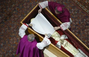 Before the wooden coffin is closed, Pope Benedict XVI’s personal secretary Archbishop Georg Gänswein and Monsignor Diego Giovanni Ravelli, the Vatican’s lead master of ceremonies for papal liturgies, place a white veil over the late pope’s face. The action on Jan. 4, 2023, is part of the funeral rites for popes. Credit: Vatican Media