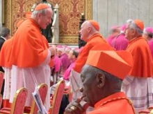 Cardinal Bernard Agre of Abidjan, Ivory Coast reads his program while Cardinal Christoph Schonborn greets a friend