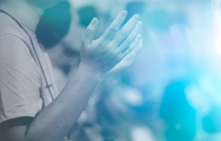 A man raises his hands in prayer.   MIA. studio/shutterstock