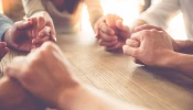 Women holding hands in prayer. Stock image via Shutterstock.