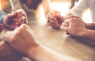 Women holding hands in prayer. Stock image via Shutterstock. null