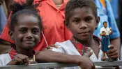 Two children, one of them holding a statue of Blessed Peter To Rot, await the visit of Pope Francis at the Caritas Technical Secondary School in Port Moresby, Papua New Guinea, Sept. 7, 2024