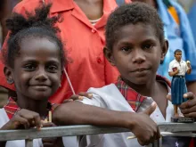 Two children, one of them holding a statue of Blessed Peter To Rot, await the visit of Pope Francis at the Caritas Technical Secondary School in Port Moresby, Papua New Guinea, Sept. 7, 2024.