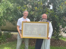 Louisiana Senator Fred Mills standing with Fr. Michael Champagne holding a framed copy of Senate Resolution No. 116. Credit: Jennifer Angelle.