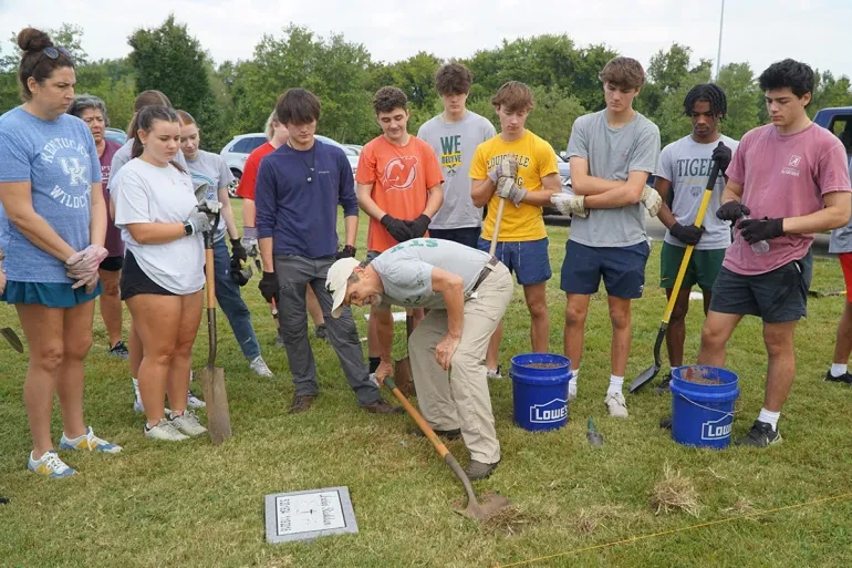 Ben Kresse, a theology teacher at St. Xavier High School, shows a group of students how to uncover a temporary marker on a gravesite in Meadow View Cemetery, Louisville, Kentucky, Sept. 21, 2024.?w=200&h=150