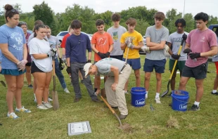 Ben Kresse, a theology teacher at St. Xavier High School, shows a group of students how to uncover a temporary marker on a gravesite in Meadow View Cemetery, Louisville, Kentucky, Sept. 21, 2024. Credit: The Record/Ruby Thomas