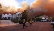 Firefighters run as a brush fire burns in Pacific Palisades, California, on Jan. 7, 2025. A fast-moving brushfire in a Los Angeles suburb burned buildings and sparked evacuations as “life-threatening” winds whipped the region.