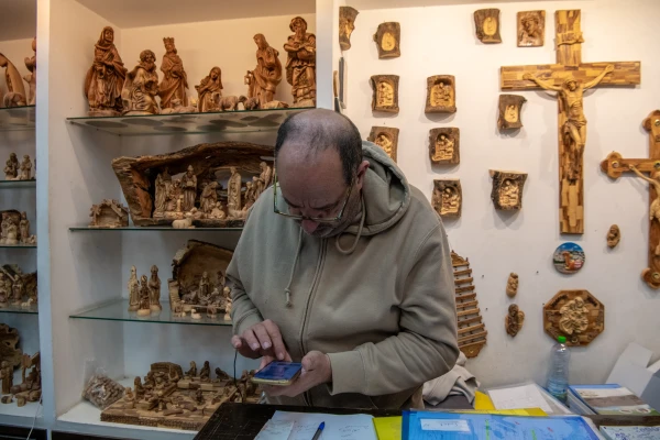 Jack Giacaman in his shop on Milk Grotto Street in Bethlehem completes an electronic payment in December 2024. For over a year, the only way to sell has been through online purchases or orders from abroad. Credit: Marinella Bandini