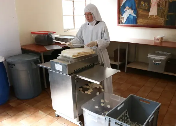 A young Carmelite nun passes the templates through a cutting machine, from which the hosts fall out. Credit: Eduardo Berdejo/EWTN News