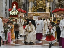 Pope Francis carries the statue of the Child Jesus to place in the Nativity scene inside St. Peter's Basilica at the end of Mass on Christmas Eve, Dec. 24, 2024, surrounded by children dressed in traditional clothing from their countries.