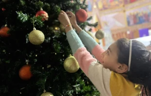 A young girl hangs an ornament on the Christmas tree inside the Church of the Holy Family in Gaza. Credit: Photo courtesy of Father Gabriel Romanelli