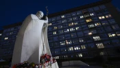 A statue of St. John Paul II is flanked by candles with images of Pope Francis placed there by those praying for the Holy Father as he is treated for pneumonia and bronchitis at Gemelli Hospital in Rome the evening of Feb. 21, 2025.