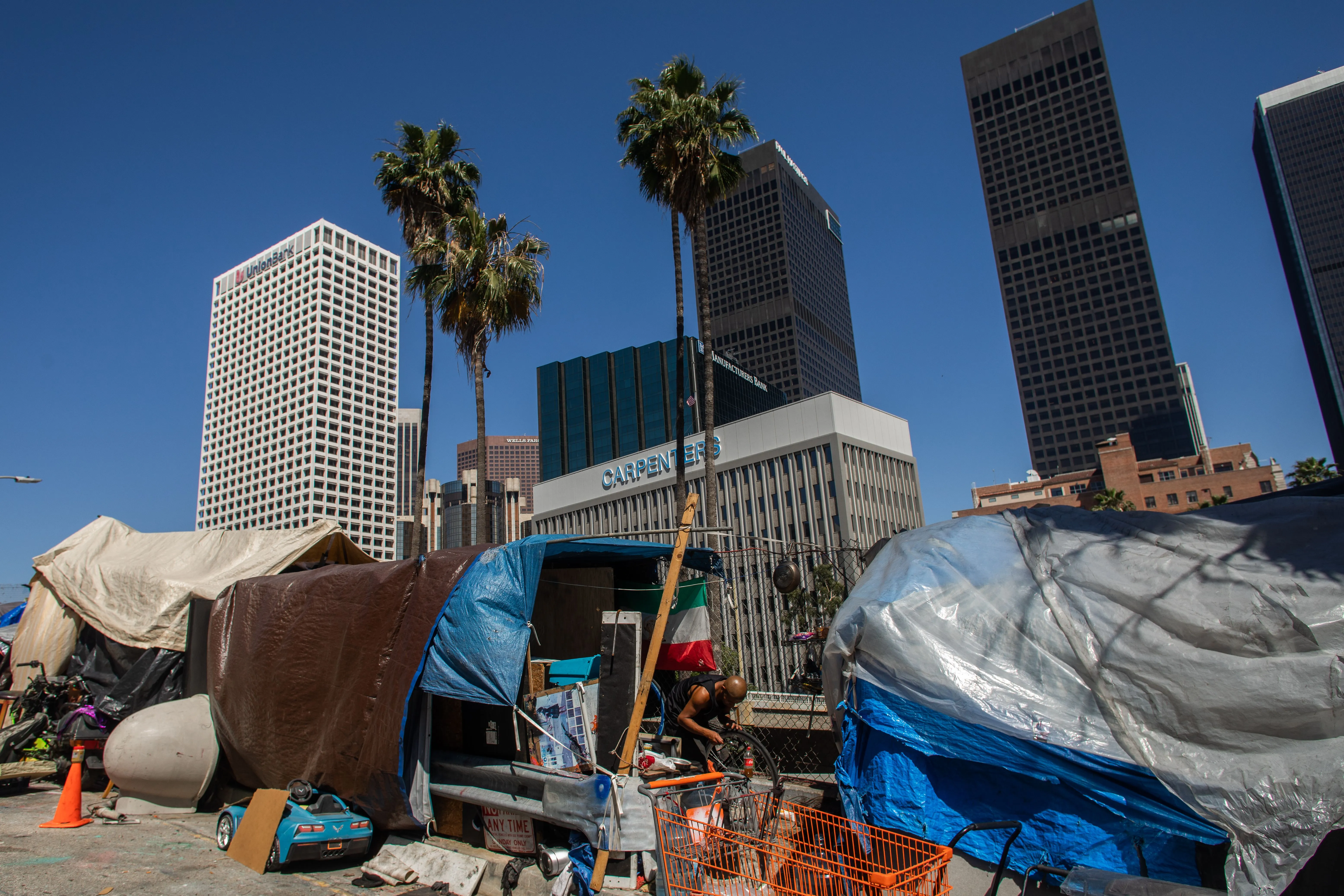 A homeless man fixes his bike outside his tent next to the 110 Freeway in Los Angeles California on May 25, 2020.?w=200&h=150