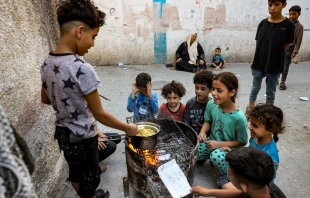 Children sit together around a boy cooking instant noodles on a fire in a makeshift oven from a recycled barrel in Rafah in the southern Gaza Strip on Oct. 31, 2023, amid ongoing battles between Israel and Hamas. Credit: MOHAMMED ABED/AFP via Getty Images