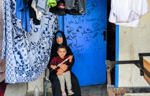 A woman sits with a child by drying laundry outside a classroom at a school run by the United Nations Relief and Works Agency for Palestine Refugees in the Near East (UNRWA) in Rafah in the southern Gaza Strip on Nov. 14, 2023, where internally displaced Palestinians have taken refuge amid ongoing battles between Israel and the Palestinian militant group Hamas. Credit: SAID KHATIB/AFP via Getty Images