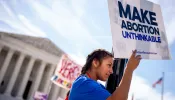 A pro-life supporter stands on a lamppost and holds a sign that reads "MAKE ABORTION UNTHINKABLE" in front of the Supreme Court on June 20, 2024, in Washington, D.C.