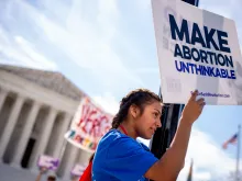 A pro-life supporter stands on a lamppost and holds a sign that reads "MAKE ABORTION UNTHINKABLE" in front of the Supreme Court on June 20, 2024, in Washington, D.C.