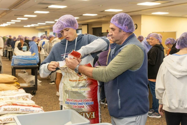 Volunteers cut open new bags of rice to refill packaging stations at St. Isidore. The entire effort took just over two hours to pack 100,000 meals in an assembly-line format. Credit: Steven Stechschulte/Special to Detroit Catholic