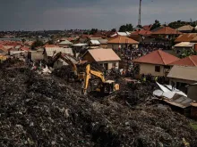 People look on as an excavator helps search for people trapped under debris after a landfill collapsed in Kampala, Uganda, on Aug. 10, 2024. Eight people including two children were killed when mountains of garbage collapsed at a landfill, the city authority said.