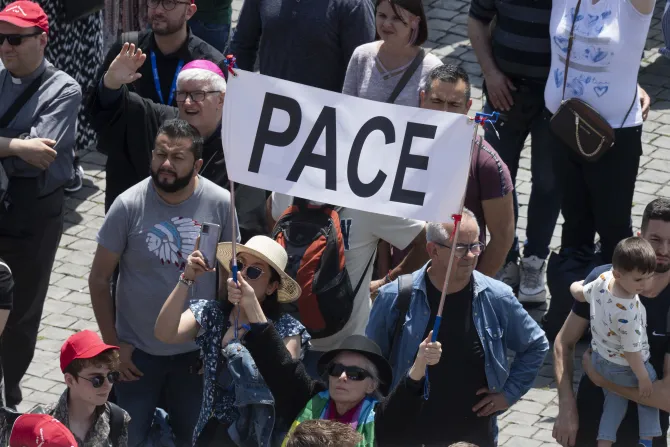 Pilgrims in St. Peter's Square hold up a sign that says "pace," which means "peace" in Italian.