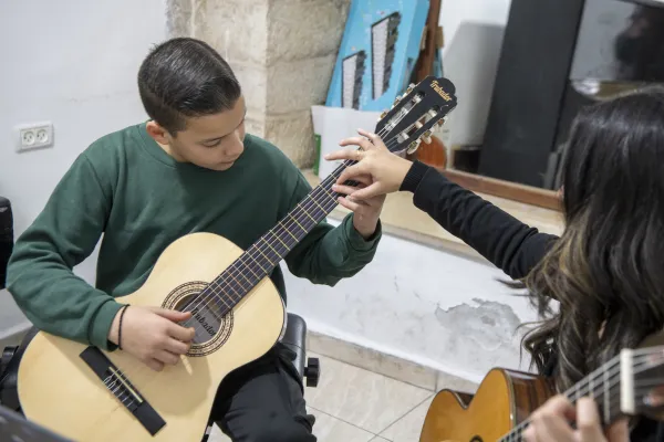 A teacher helps a boy properly position his fingers on the guitar neck during a guitar lesson at the Magnificat Institute in Jerusalem. "Sometimes they may work together as adults, but the type of relationship is always employer-employee. Here, however, it’s a teacher-student relationship, which is qualitatively very different and presupposes an emotional involvement that is not present in other contexts." Credit: Photo courtesy of Silvia Giuliano/Custody of the Holy Land
