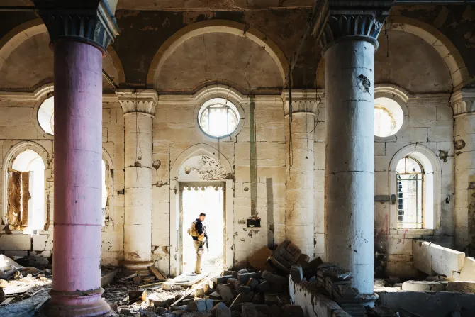 An unknown security guard stands at the entrance of a church destroyed during the fighting with ISIS in Mosul, Iraq.