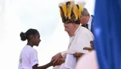 Pope Francis wears a traditional head dress as greets a young girl in Vanimo, Papua New Guinea, Sept. 8, 2024.