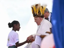 Pope Francis wears a traditional head dress as greets a young girl in Vanimo, Papua New Guinea, Sept. 8, 2024.